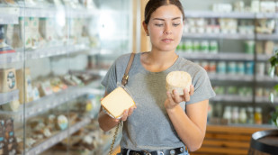 Frau in der Käseabteilung schaut sich zwei Käseverpackungen an Frau in der Käseabteilung schaut sich zwei Käseverpackungen an